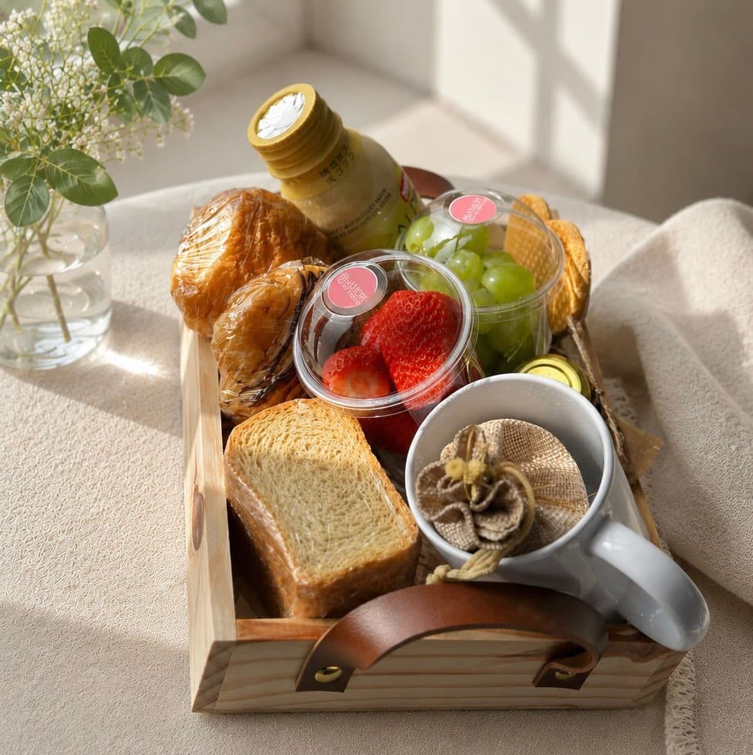 Cesta de café da manhã em bandeja de madeira com pães, frutas, suco e caneca personalizada.